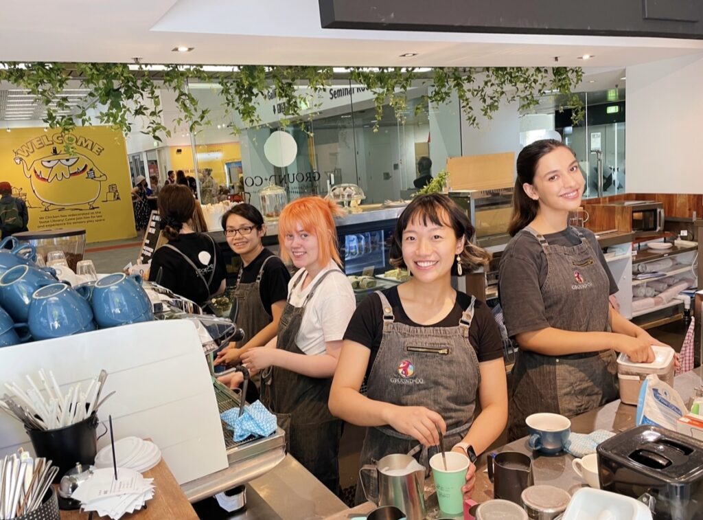 5 Ground+Co staff behind the coffee machine at the cafe smiling at the camera